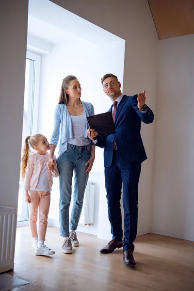 Handsome broker showing room while standing near attractive woman and kid — Stock Photo