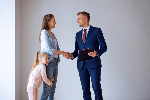 Handsome broker shaking hands with attractive woman standing with cute daughter — Stock Photo