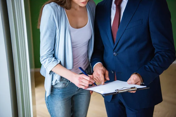 Vue recadrée de la femme signant le document tout en se tenant près du courtier dans une nouvelle maison — Photo de stock