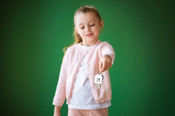 Selective focus of kid holding house shaped key chain on green background — Stock Photo