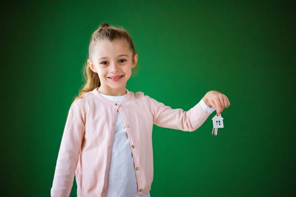 Enfant souriant tenant porte-clés en forme de maison sur fond vert — Photo de stock