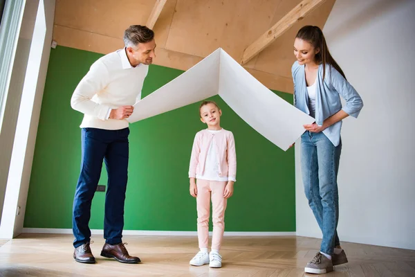 Весела дочка стоїть під паперовим дахом в руках щасливих батьків — стокове фото