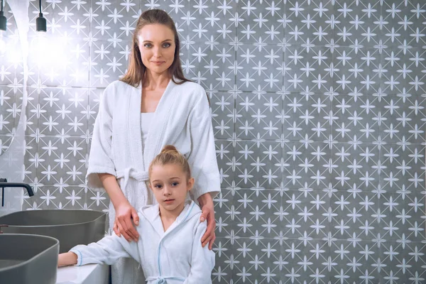 Attrayant femme debout avec fille mignonne en peignoirs de bain — Photo de stock