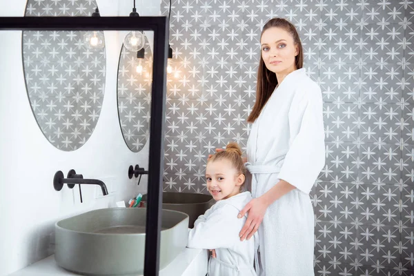 Bela mulher de pé com filha adorável em roupões de banho — Fotografia de Stock