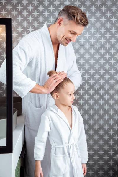 Feliz padre haciendo pelo de linda hija de pie en el baño - foto de stock
