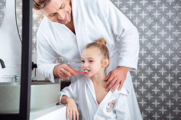 Feliz padre ayudando a hija cepillarse los dientes en el baño - foto de stock