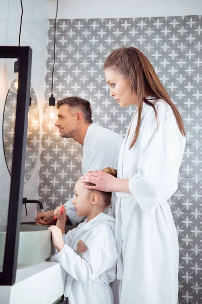 Hombre de pie cerca de la esposa con hija sosteniendo el cepillo de dientes en el baño - foto de stock