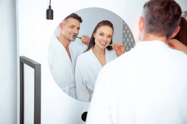 Alegre casal escovação dentes e olhando no espelho no banheiro — Fotografia de Stock