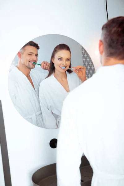 Cheerful couple brushing teeth and looking in mirror in bathroom — Stock Photo