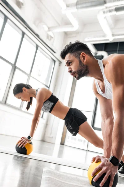 Muscoloso giovane uomo e ragazza sportiva che si esercita con palle di medicina su stuoie di yoga — Foto stock