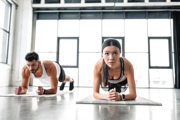 Athletic young man and woman in sportswear doing plank exercise on yoga mats in gym — Stock Photo