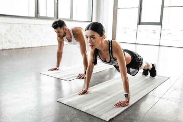 Deportivo joven pareja haciendo flexiones en yoga esteras en gimnasio - foto de stock