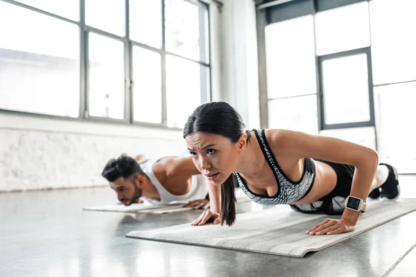Athletic concentrated young woman and man doing push ups on yoga mats in gym — Stock Photo