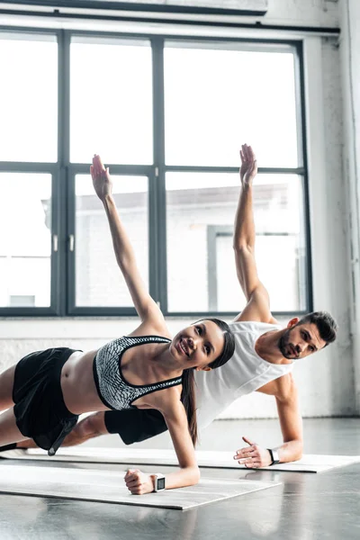 Glückliches, sportliches junges Paar macht Seitenplanken-Gymnastik auf Yogamatten im Fitnessstudio — Stockfoto