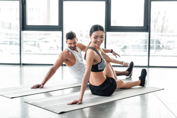 Happy young couple sitting on yoga mats and stretching in gym — Stock Photo