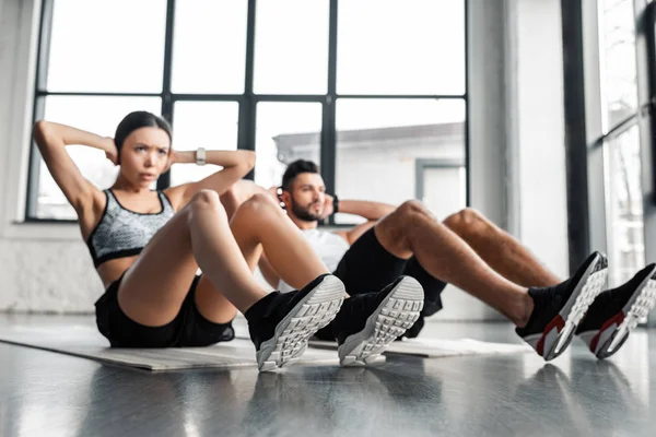 Молодая пара делает упражнения на прессе на ковриках для йоги в тренажерном зале — стоковое фото