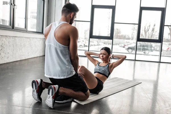 Allenatore di sesso maschile che aiuta la giovane sportiva a fare esercizio addominale in palestra — Foto stock