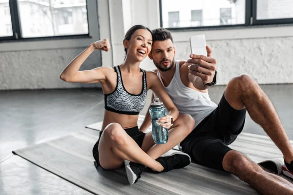 Щасливі молода пара в спортивному одязі, беручи selfie з смартфон під час відпочинку на йога килимки після тренування в тренажерному залі — стокове фото