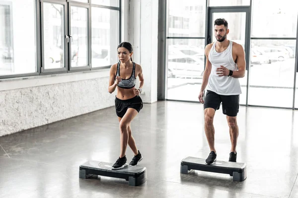 Muscular young man and beautiful sporty girl exercising together on step platforms in gym — Stock Photo