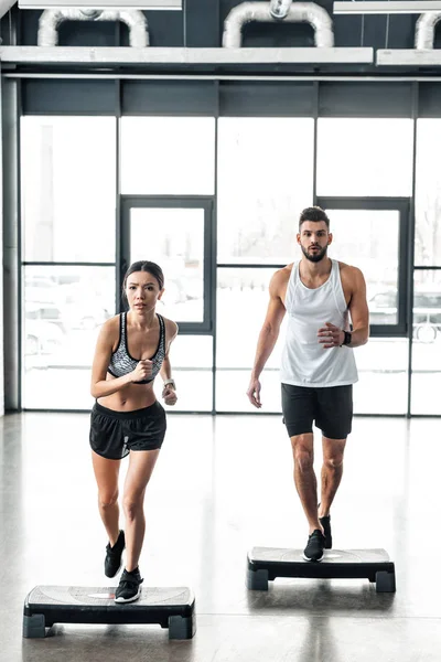 Vue complète du jeune couple sportif s'exerçant sur des plates-formes pas à pas dans la salle de gym — Photo de stock