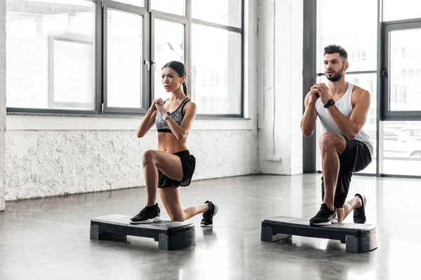 Muscular young man and beautiful sporty girl training on step platforms in gym — Stock Photo