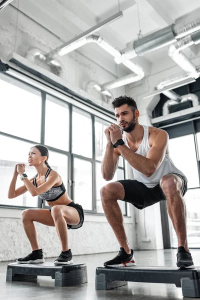 Vue à faible angle du jeune couple athlétique dans l'entraînement de vêtements de sport avec des plates-formes pas à pas dans la salle de gym — Photo de stock