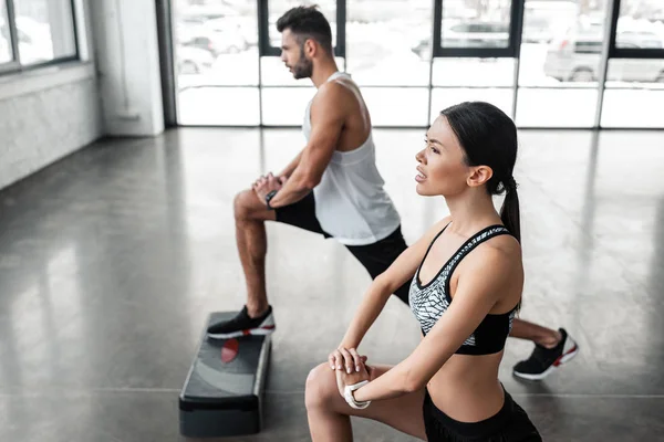Vue grand angle de jeune couple athlétique en vêtements de sport travaillant ensemble dans la salle de gym — Photo de stock