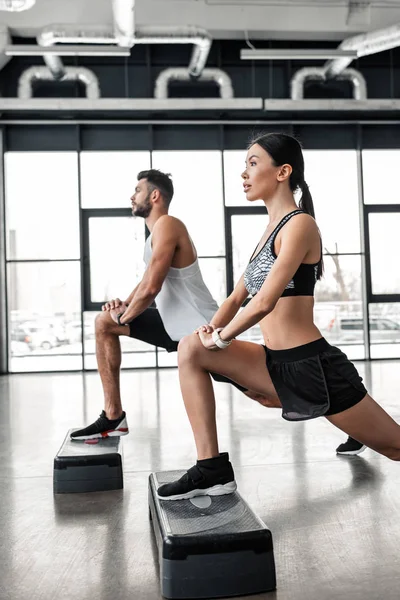 Side view of athletic young man and woman training with step platforms in gym — Stock Photo