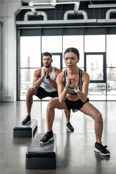 Vue pleine longueur de concentré jeune couple exerçant avec des plates-formes pas à pas dans la salle de gym — Photo de stock