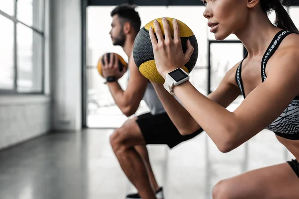 Plan recadré de jeune couple sportif tenant des boules de médecine et s'entraînant ensemble dans la salle de gym — Photo de stock