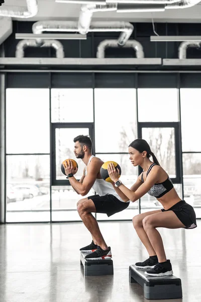 Vista laterale della giovane coppia atletica in allenamento di abbigliamento sportivo con piattaforme passo in palestra — Foto stock