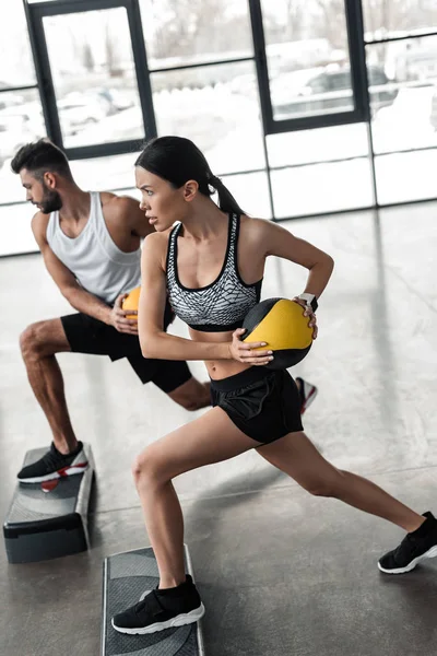 Athletic young couple in sportswear training with step platforms in gym — Stock Photo