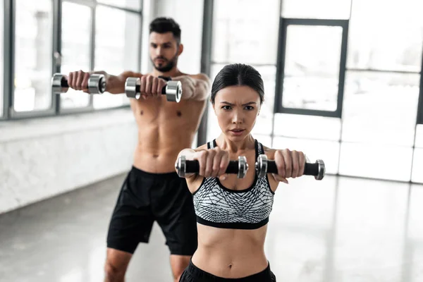 Young sporty man and woman holding dumbbells and training together in gym — Stock Photo