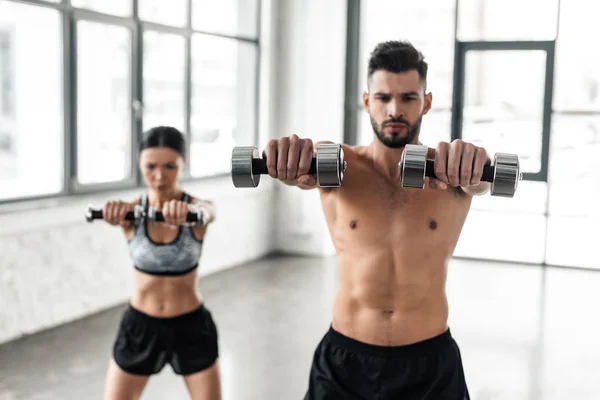 Sporty young couple exercising with dumbbells in gym — Stock Photo