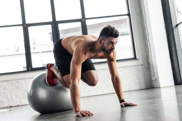 Giovane sportivo a petto nudo che si esercita sulla palla fitness in palestra — Foto stock