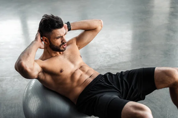 Hochwinkelaufnahme eines jungen Sportlers mit nacktem Oberkörper beim Bauchmuskeltraining auf dem Fitnessball im Fitnessstudio — Stockfoto