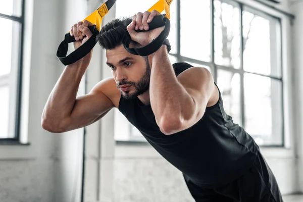 Schöner, konzentrierter, sportlicher Mann, der an Widerstandsbändern hängt und im Fitnessstudio wegschaut — Stockfoto