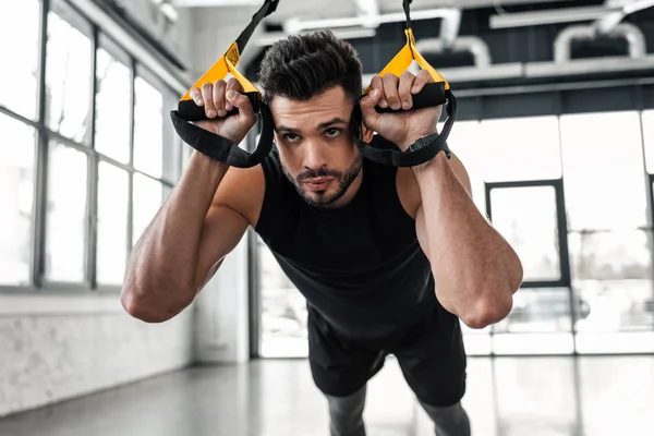 Handsome concentrated sporty man hanging and training with fitness straps in gym — Stock Photo