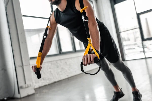 Cropped shot of muscular young man in sportswear exercising with resistance bands in gym — Stock Photo