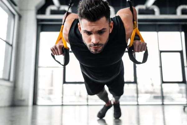 Focused muscular young sportsman exercising with suspension straps in gym — Stock Photo