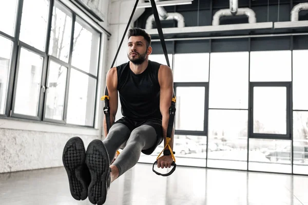 Handsome muscular young sportsman exercising with suspension straps in gym — Stock Photo