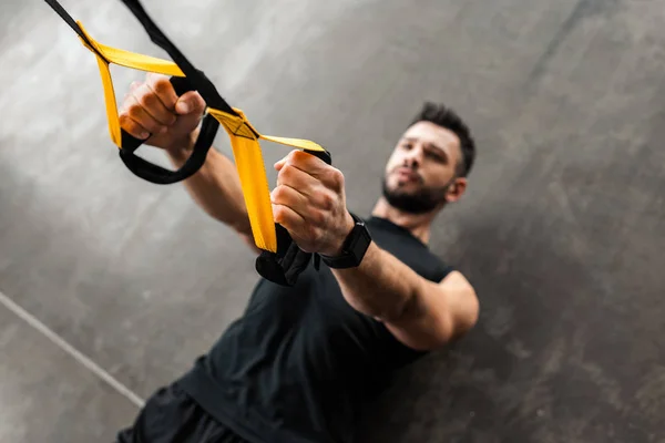 High angle view of muscular young man in sportswear hanging and training with resistance bands in gym — Stock Photo