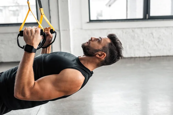 Side view of athletic young man in sportswear hanging and training with resistance bands in gym — Stock Photo