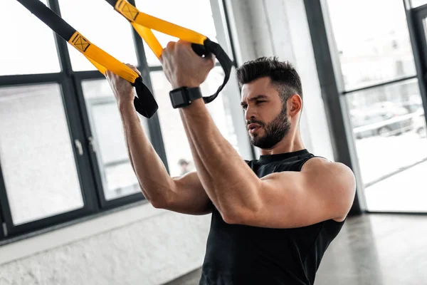 Athletic muscular young man in sportswear training with suspension straps in gym — Stock Photo