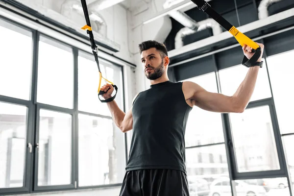 Low angle view of athletic young man in sportswear training with suspension straps in gym — Stock Photo