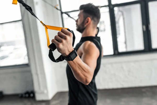 Visão lateral do jovem musculoso no treinamento de sportswear com bandas de resistência no ginásio — Fotografia de Stock