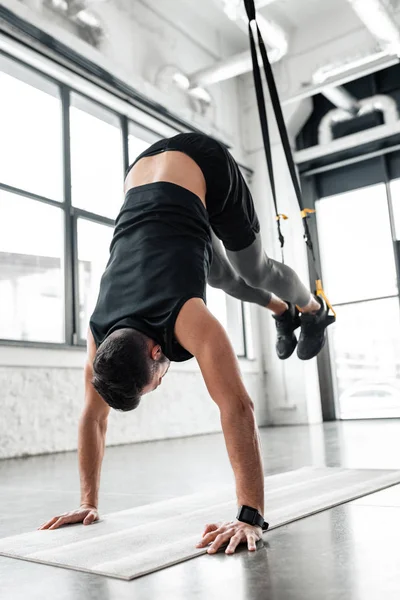 Young sportsman performing handstand on yoga mat and training with resistance bands in gym — Stock Photo