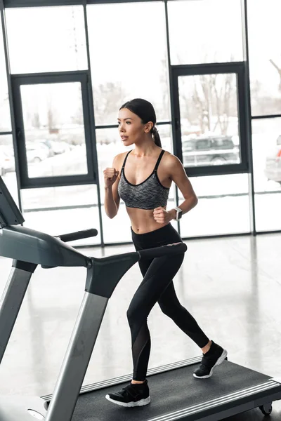 Beautiful young sportswoman running on treadmill in gym — Stock Photo