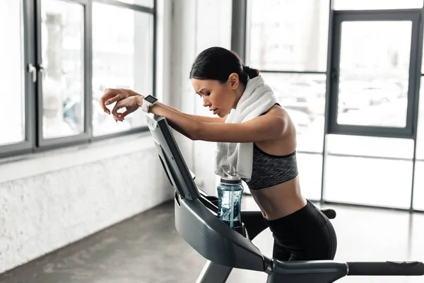 Side view of tired young sportswoman with towel around neck leaning at treadmill after workout in gym — Stock Photo