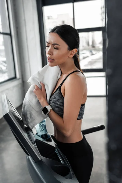 Müde junge Sportlerin wischt Schweiß mit Handtuch ab und steht nach dem Training im Fitnessstudio auf dem Laufband — Stockfoto